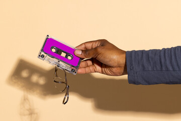 Close up of hand of african american man holding purple cassette tape over beige background