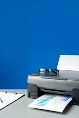 Laser printer on desk against blue background.