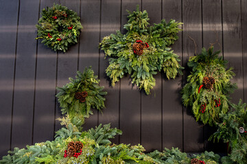 Snowflake shaped fresh Christmas wreath make out of evergreen branches, pinecones and red berries, hanging on a wood wall
