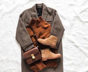 Seasonal women's clothing - coat, cashmere sweater, suede boots, crossbody bag on a light background, top view