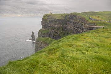 cliffs landscape with castle, green meadow and gray sky in ireland
