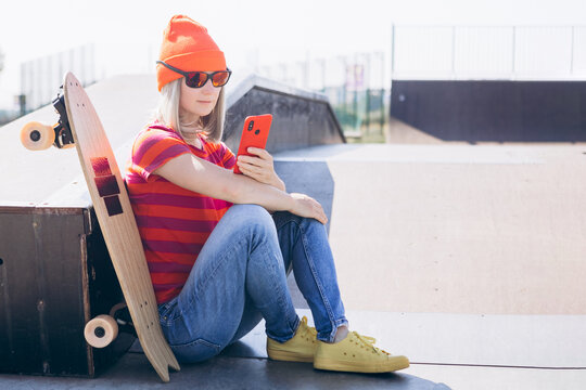 Beautiful young hipster woman using smart phone On Skateboard at summer day. Active lifestyle, modern life, subculture concept - Powered by Adobe
