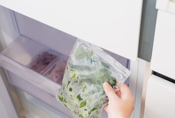 Female hand takes out a plastic bag with frozen spinach from the refrigerator, close-up.