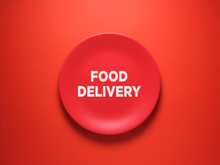 The word Food Delivery on ceramic red plate over red background.