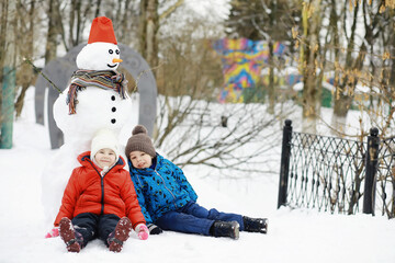 Children in the park in winter. Kids play with snow on the playground. They sculpt snowmen and...