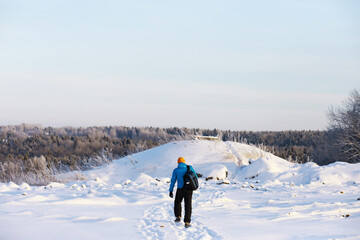 Hiking winter landscape. A man with a backpack travels in winter. A man in a snowy field.