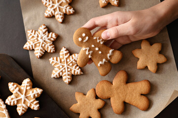 Person's hands holding gingerbread man cookie, various cookies on table, on baking paper background. Traditional Christmas home dessert. Top view, soft selective focus, lifestyle