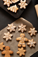 Traditional Christmas gingerbread cookies in various shapes, on brown baking paper on dark table background. Holiday winter European food, top view, lifestyle, selective focus
