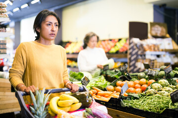 Woman shopping at store, walking among shelves and choosing products