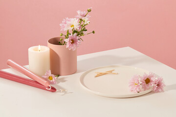Obraz na płótnie Canvas On the white table there are candles, fresh flowers, a ceramic cup and a ceramic plate with a pink background. Space for product display. Beauty theme.