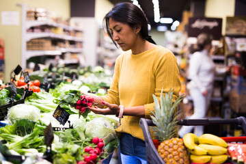 Woman shopper chooses ripe radish at grocery supermarket