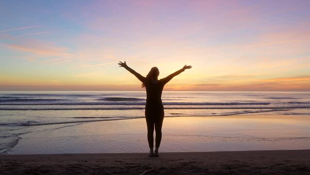 silhouette of woman spreading her arms and watching the sea at sunrise