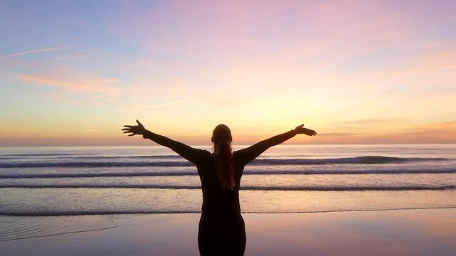 woman spreading her arms and watching the sea at sunrise with zoom out
