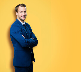 Portrait of smiling businessman in suit and tie, with crossed arms, isolated against vivid yellow...