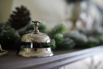 Ringing reception bell on desk of guesthouse, hotel at christmas time. Color shining garland on christmas tree on background. Travel concept.