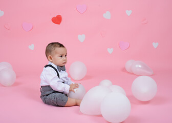 Fototapeta na wymiar Baby sitting on pink background with balloons. Valentine's day background.