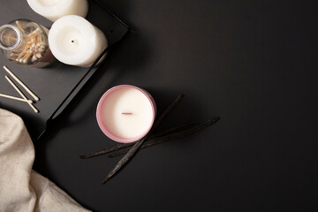 Two white candles and a bottle of cotton swabs are displayed on a black tray. A jar of scented...
