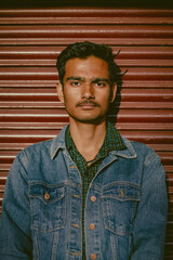 Close up shot of a model, posing with denim jacket and black sunglasses with selective focus. Handsome indian model standing near a wall. Smart,dashing indian men in fashionable outfit. 