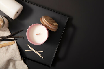 Scented candles, cotton swabs and cloths are displayed on trays against a black background. A...