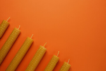 Stylish elegant beeswax candles, wax sheets on orange background. Top view, flat lay. Space for...
