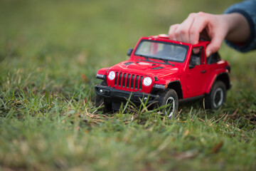 a red toy off-road vehicle pushed on the grass by the hand of a little boy