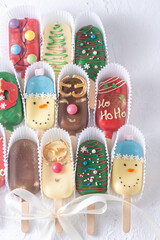 Christmas dessert. Sweet food. Cheesecake on a stick in the shape of ice cream. Children's treat in winter. Candy Christmas tree, snowman, deer and Santa Claus. Gingerbread cookies background.