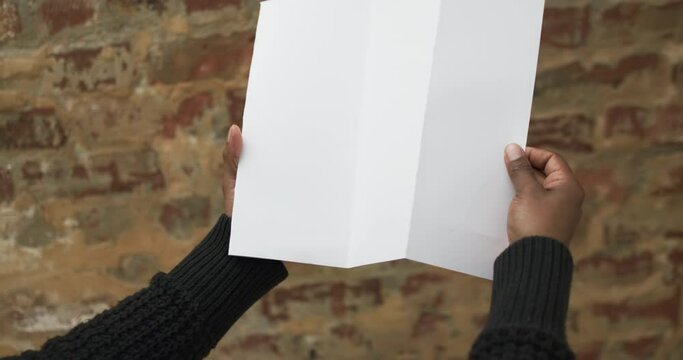 Video of hand of african american man holding white blank page, copy space over brick wall