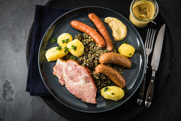 Oldenburger Grünkohl mit geräucherter Kohlwurst, Pinkel, Kassler Nacken, Kartoffeln, Senf, Petersilie auf Teller und dunkel schwarz Schiefer Hintergrund