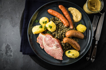 Oldenburger Grünkohl mit geräucherter Kohlwurst, Pinkel, Kassler Nacken, Kartoffeln, Senf, Petersilie auf Teller und dunkel schwarz Schiefer Hintergrund