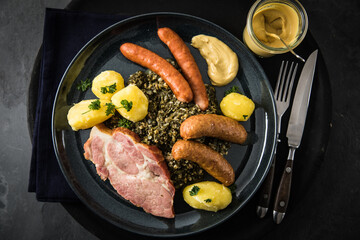 Oldenburger Grünkohl mit geräucherter Kohlwurst, Pinkel, Kassler Nacken, Kartoffeln, Senf, Petersilie auf Teller und dunkel schwarz Schiefer Hintergrund