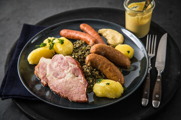 Oldenburger Grünkohl mit geräucherter Kohlwurst, Pinkel, Kassler Nacken, Kartoffeln, Senf, Petersilie auf Teller und dunkel schwarz Schiefer Hintergrund