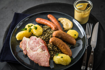 Oldenburger Grünkohl mit geräucherter Kohlwurst, Pinkel, Kassler Nacken, Kartoffeln, Senf, Petersilie auf Teller und dunkel schwarz Schiefer Hintergrund