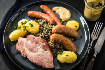 Oldenburger Grünkohl mit geräucherter Kohlwurst, Pinkel, Kassler Nacken, Kartoffeln, Senf, Petersilie auf Teller und dunkel schwarz Schiefer Hintergrund