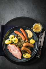 Oldenburger Grünkohl mit geräucherter Kohlwurst, Pinkel, Kassler Nacken, Kartoffeln, Senf, Petersilie auf Teller und dunkel schwarz Schiefer Hintergrund