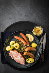 Oldenburger Grünkohl mit geräucherter Kohlwurst, Pinkel, Kassler Nacken, Kartoffeln, Senf, Petersilie auf Teller und dunkel schwarz Schiefer Hintergrund