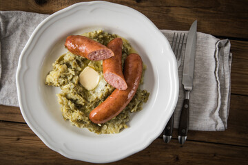 Schnibbelbohnen Eintopf aus fermentierten Stangenbohnen und Kartoffeln mit Mettwurst und zerlassener Butter auf Teller mit Besteck, Leinen Serviette und rustikalen Holz Hintergrund
