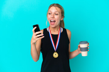 Young caucasian woman with medals isolated on blue background holding coffee to take away and a mobile
