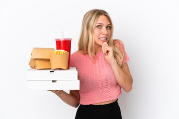 Young caucasian woman holding fat food isolated on blue background having doubts
