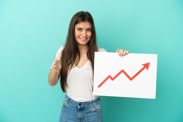Young caucasian woman isolated on blue background holding a sign with a growing statistics arrow...