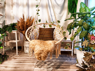 A modern cozy beautiful room with a braided rope macrame chair, green plants and a window with...