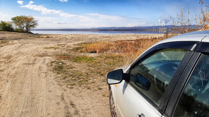 A view of a car on a sandy road and a lake, river or sea in the background. The concept of a summer...
