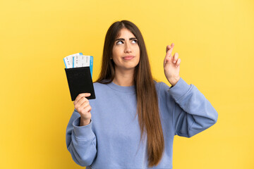 Naklejka premium Young caucasian woman holding a passport isolated on yellow background with fingers crossing and wishing the best