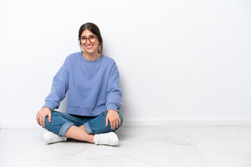 Young caucasian woman sitting on the floor isolated on white background with arms crossed and...