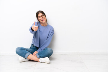 Young caucasian woman sitting on the floor isolated on white background with thumbs up because...