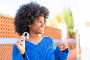 African American girl holding invisible braces at outdoors pointing to the side to present a product