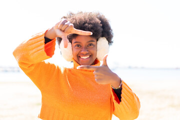 African American girl wearing winter muffs at outdoors focusing face. Framing symbol