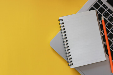 close up top view on white blank notebook with pencil and keyboard laptop on yellow background for reminder and note about plan , work and management schedule time concept