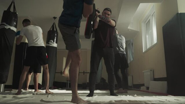 Man holds pad while partner does kicks in sports club. Kick-boxers improve fight technique together in fighting gym slow motion. Martial arts workout