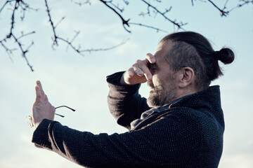 Portrait of a bearded middle-aged man with glasses in hand, covering his arm from the bright sun.
