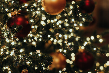 Abstract blurred Christmas tree branches with golden red glossy Christmas balls and garland lights....